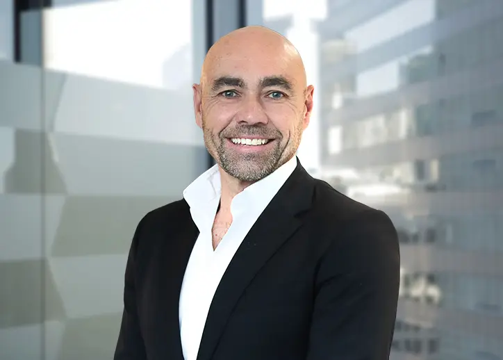 A photo of Peter Tracey looking straight ahead with a view of Sydney in the background