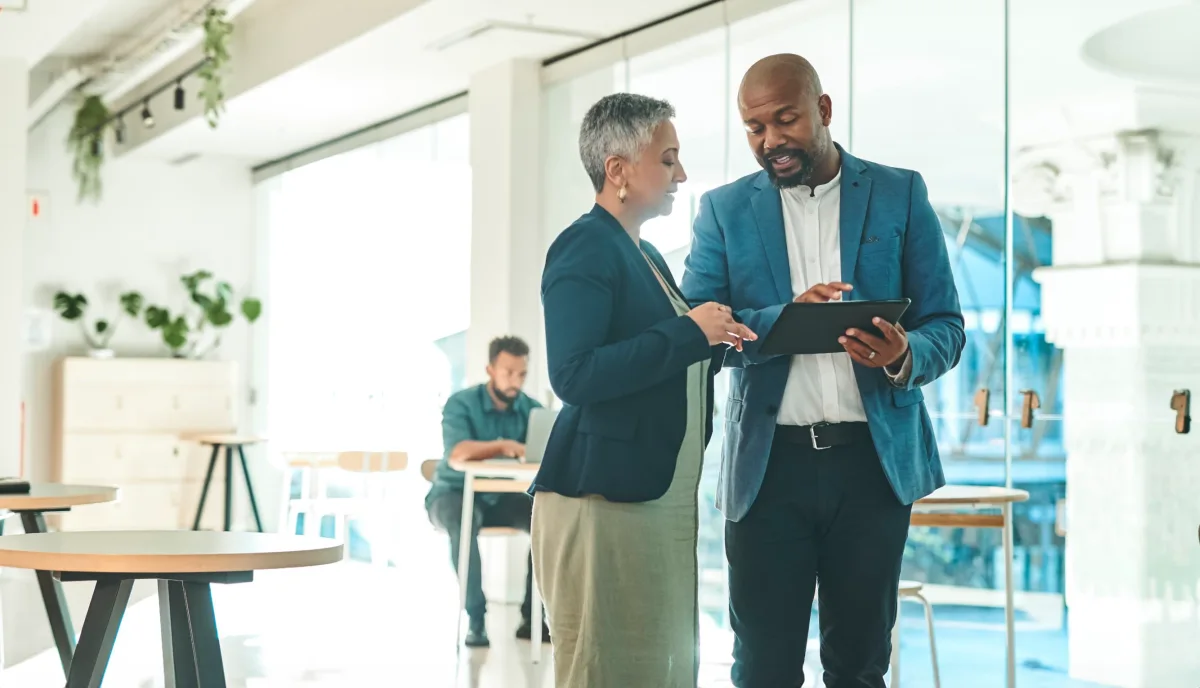 Photo of two people talking with one holding a tablet.