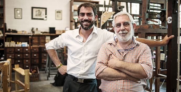 A son stands behind his father in the family workshop